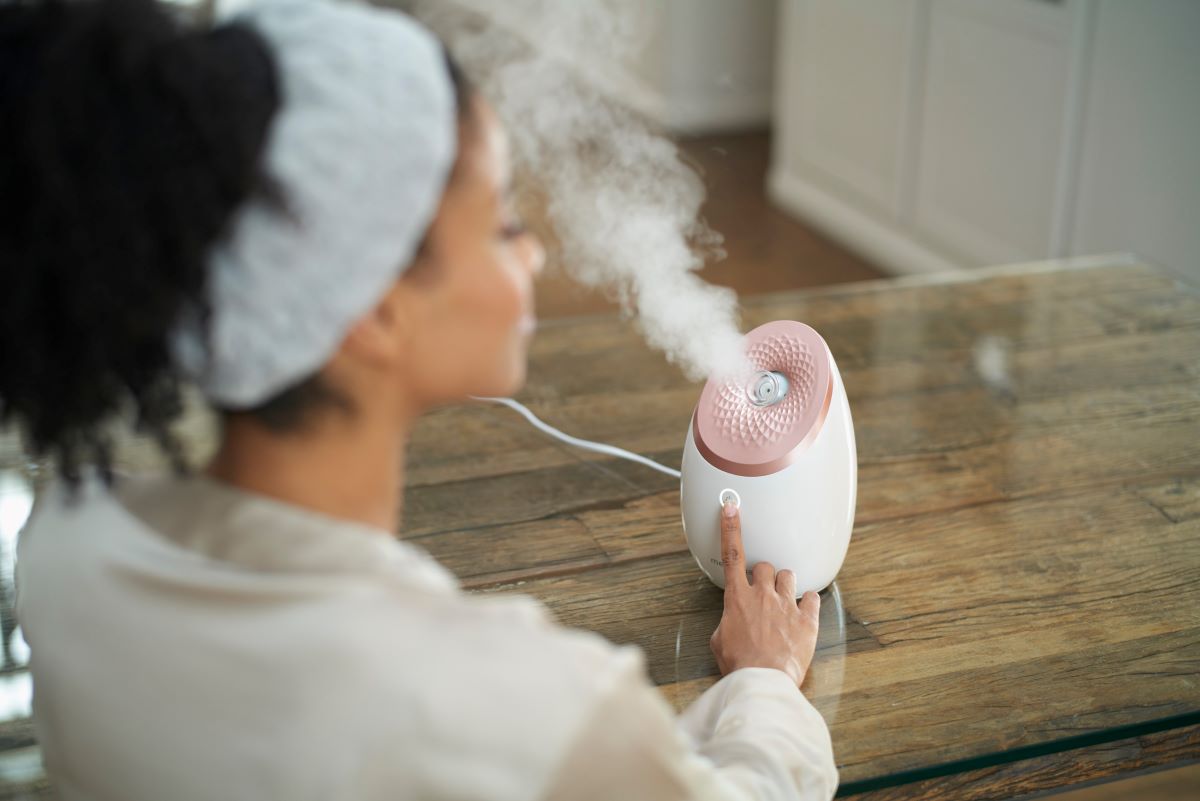 Woman with a towel around her hair using a medisana facial sauna for gentle steam treatment.